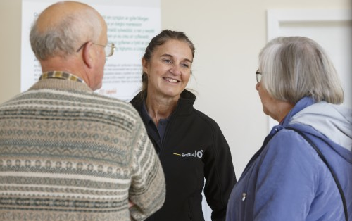 Woman in EnBW jacket talking to two older adults indoors