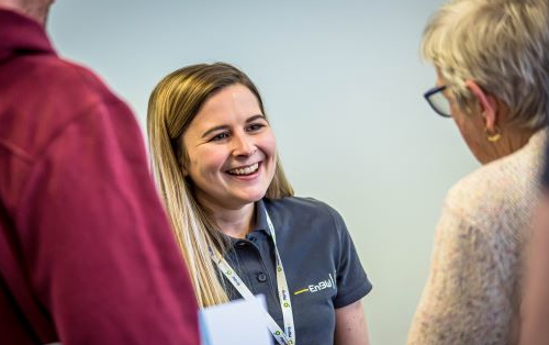 Smiling woman in EnBW polo shirt talking to two people