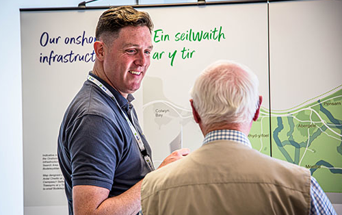 Two men discussing in front of an informational display about onshore infrastructure