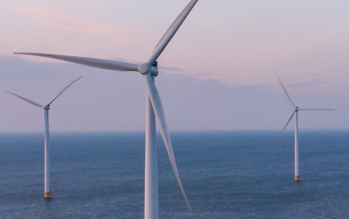 Three offshore wind turbines in the ocean at sunset
