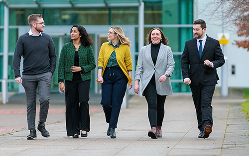 Five professionals walking outdoors in business attire near a modern building