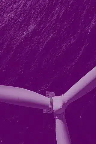 Close-up of a wind turbine rotor against a purple ocean background