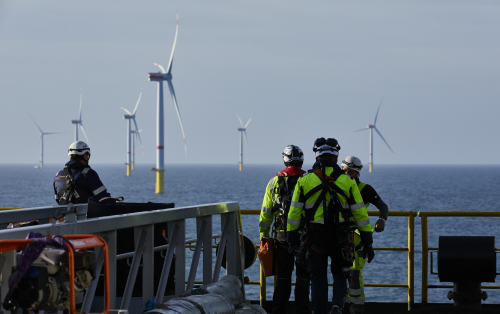 Workers in safety gear overlooking offshore wind turbines at sea
